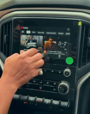 Mão tocando o YouTube aberto na tela do carro